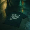 T-shirt reading "Reality Called. I Hung Up." lying on wet pavement with neon reflections at night.
