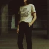 Woman wearing a beige t-shirt reading I Had Potential. Then Life Happened standing in a dim urban space.